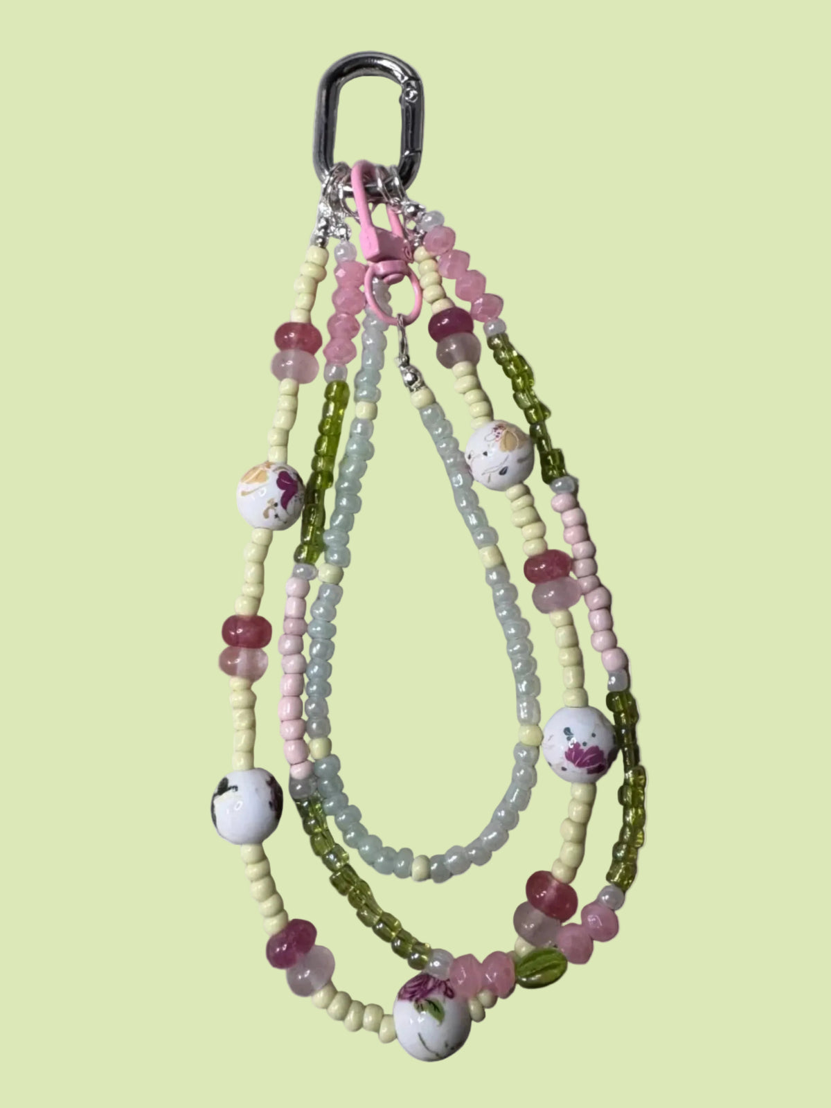Handmade beaded bag charm keychain with a silver carabiner clip, featuring pastel pink, light green, and pale yellow beads, floral accents, and small white beads with pink details.