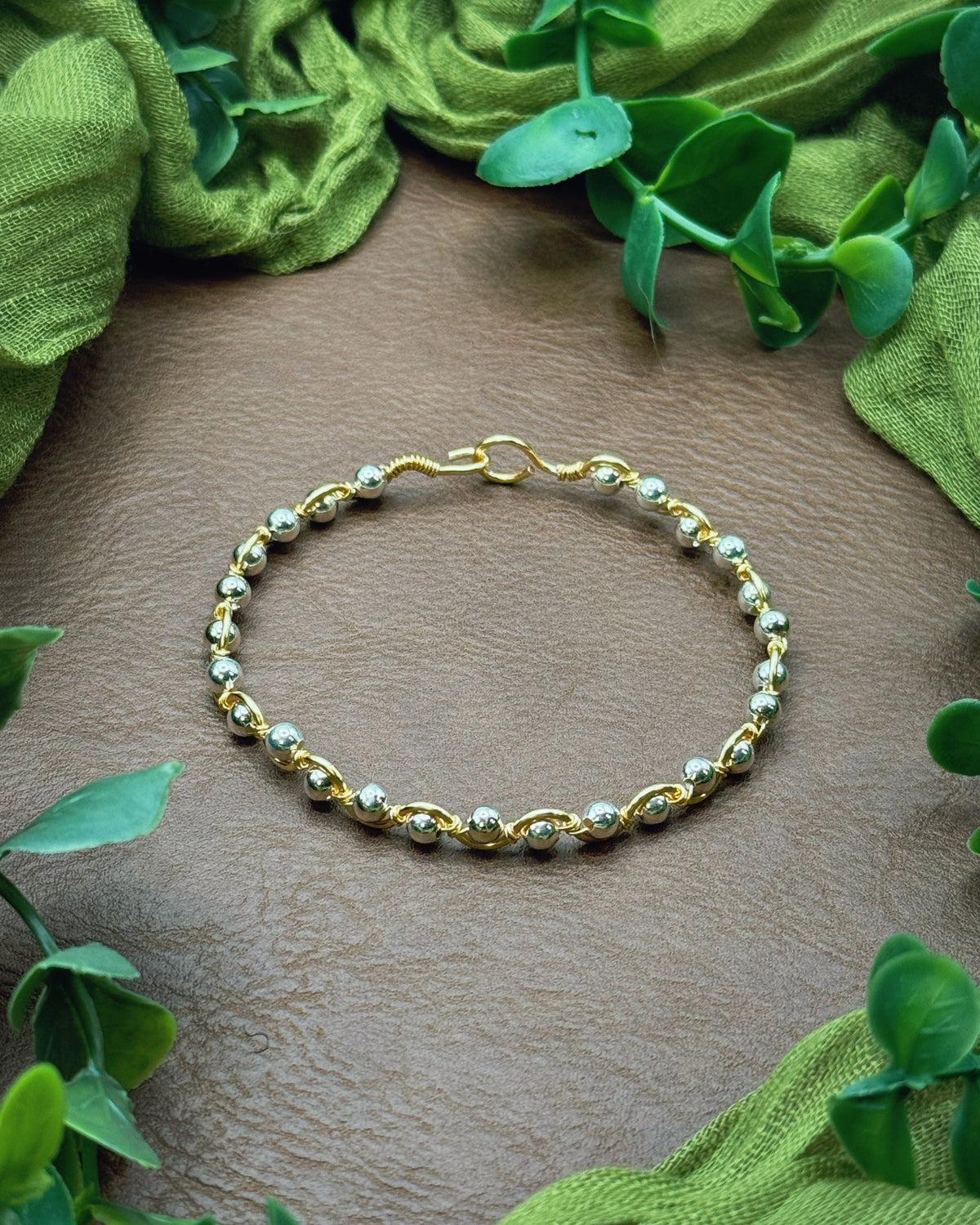 Handmade, wire-wrapped bracelet shaped like a wave, featuring silver beads.