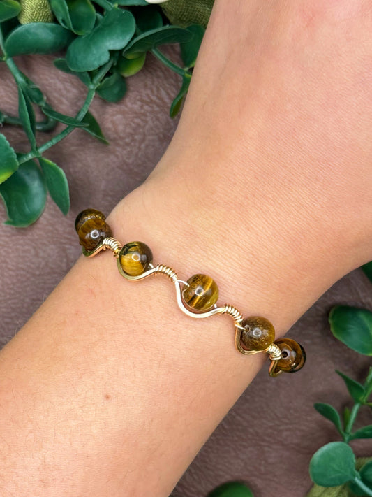 Handmade, wire-wrapped bracelet shaped like a wave, featuring tigers eye gemstone beads.
