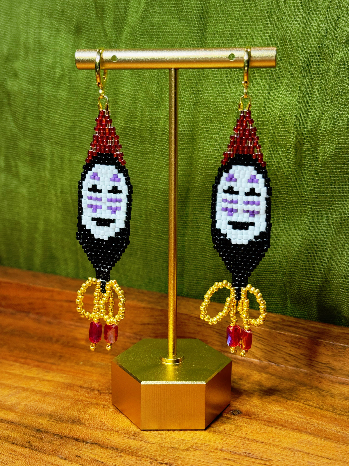 Pair of beaded earrings on a gold stand with a green background.