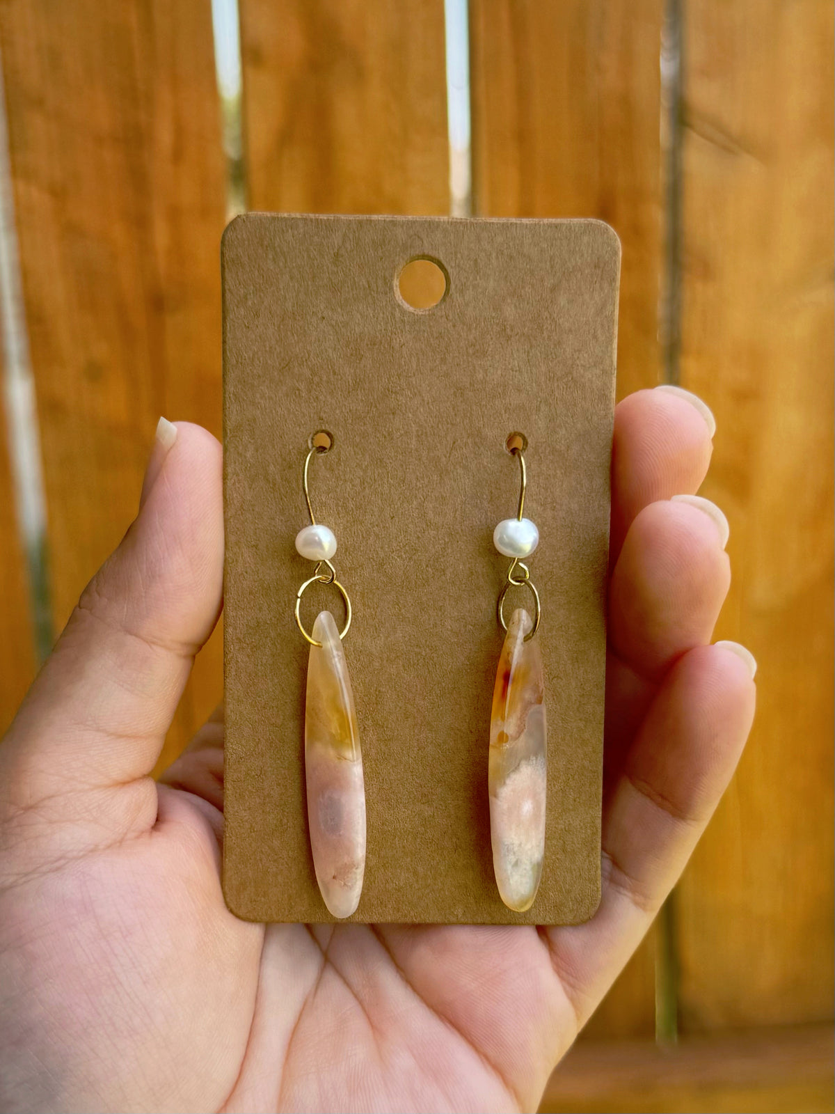 Handmade earrings with sakura agate teardrop beads, a dainty freshwater pearl, and gold ear hooks, on a kraft paper card.