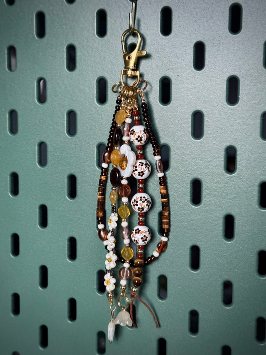 Handmade beaded bag charm keychain with round ceramic beads, white flowers, and tiger's eye beads.