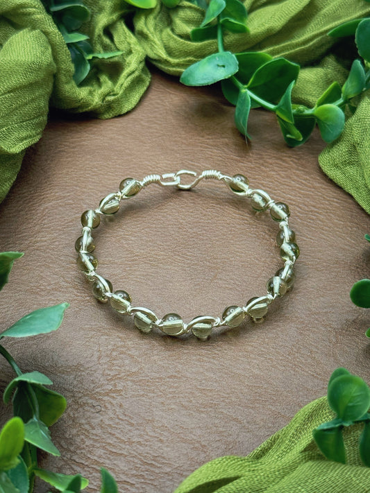 Handmade, wire-wrapped bracelet shaped like a wave, featuring smoky clear glass beads.