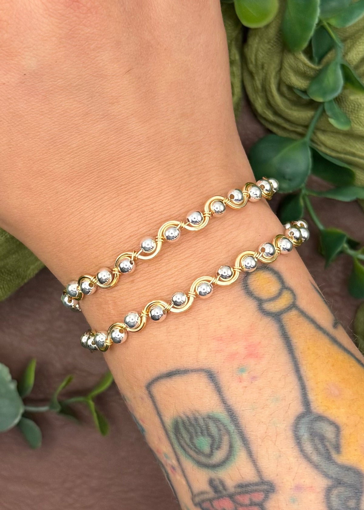 Handmade, wire-wrapped bracelet shaped like a wave, featuring silver beads.