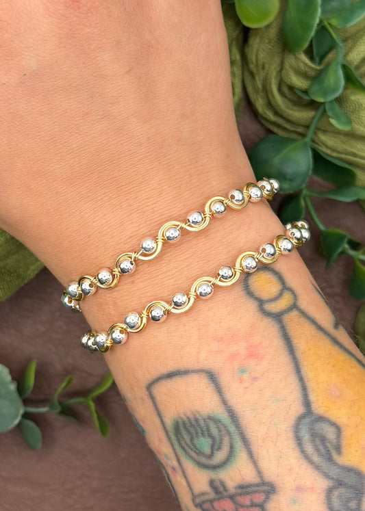 Handmade, wire-wrapped bracelet shaped like a wave, featuring silver beads.