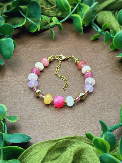 Handmade beaded bracelet with multicolored gemstone beads and gold hardware, arranged on a natural surface with green leaves.