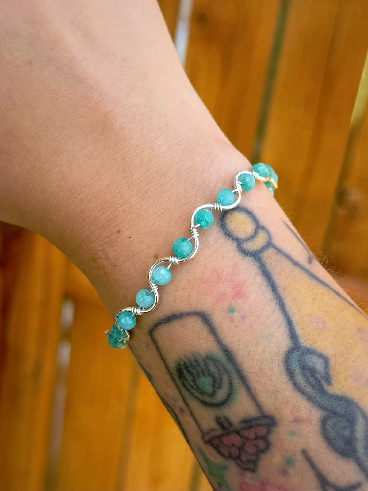 Handmade silver wire-wrapped bracelet with round aqua stone beads worn with a wooden fence background.