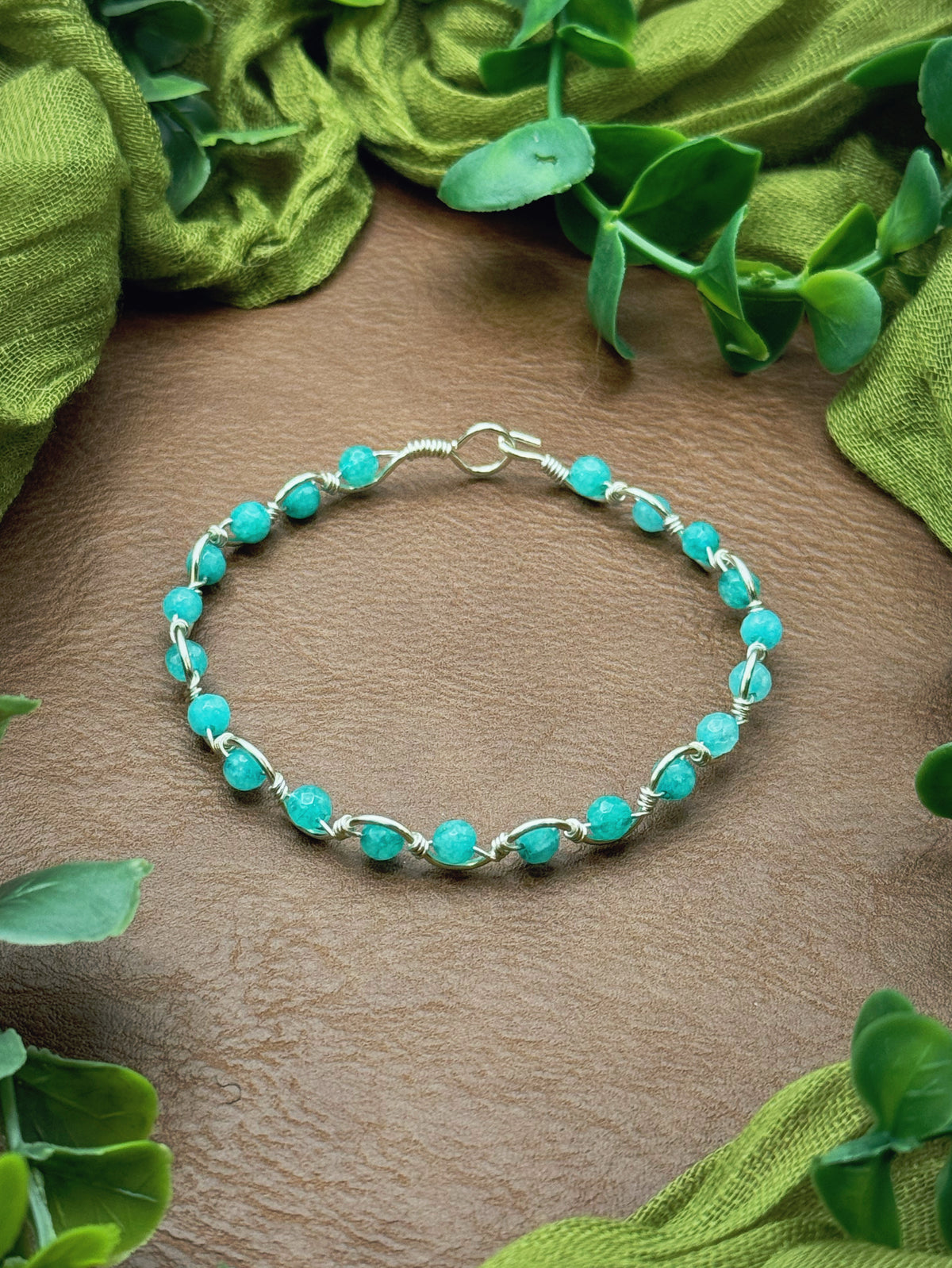 Handmade, wire-wrapped bracelet shaped like a wave, featuring aqua gemstone beads.