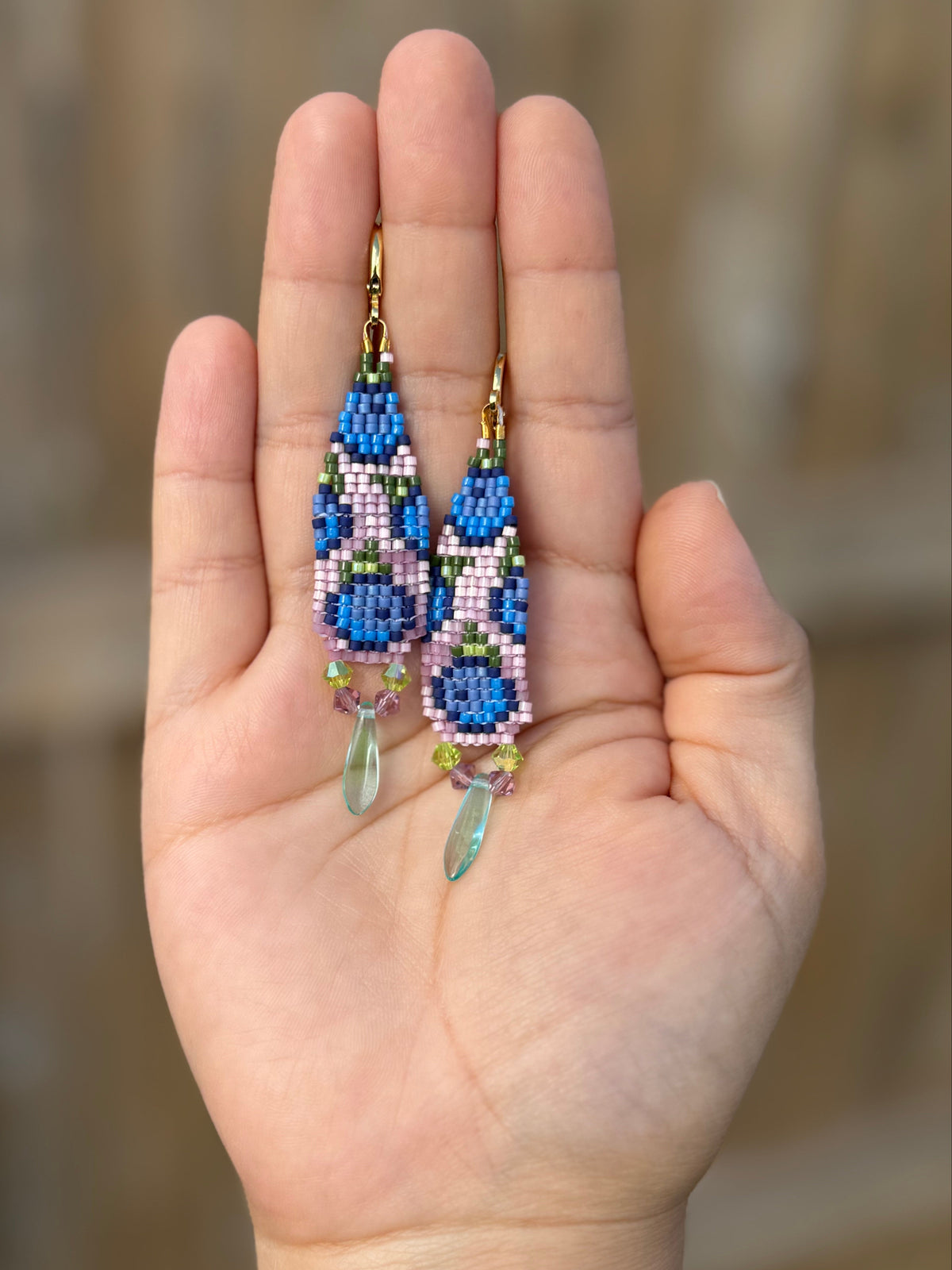 Hand holding a pair of handmade beaded earrings with Miyuki Delica and Czech glass beads.