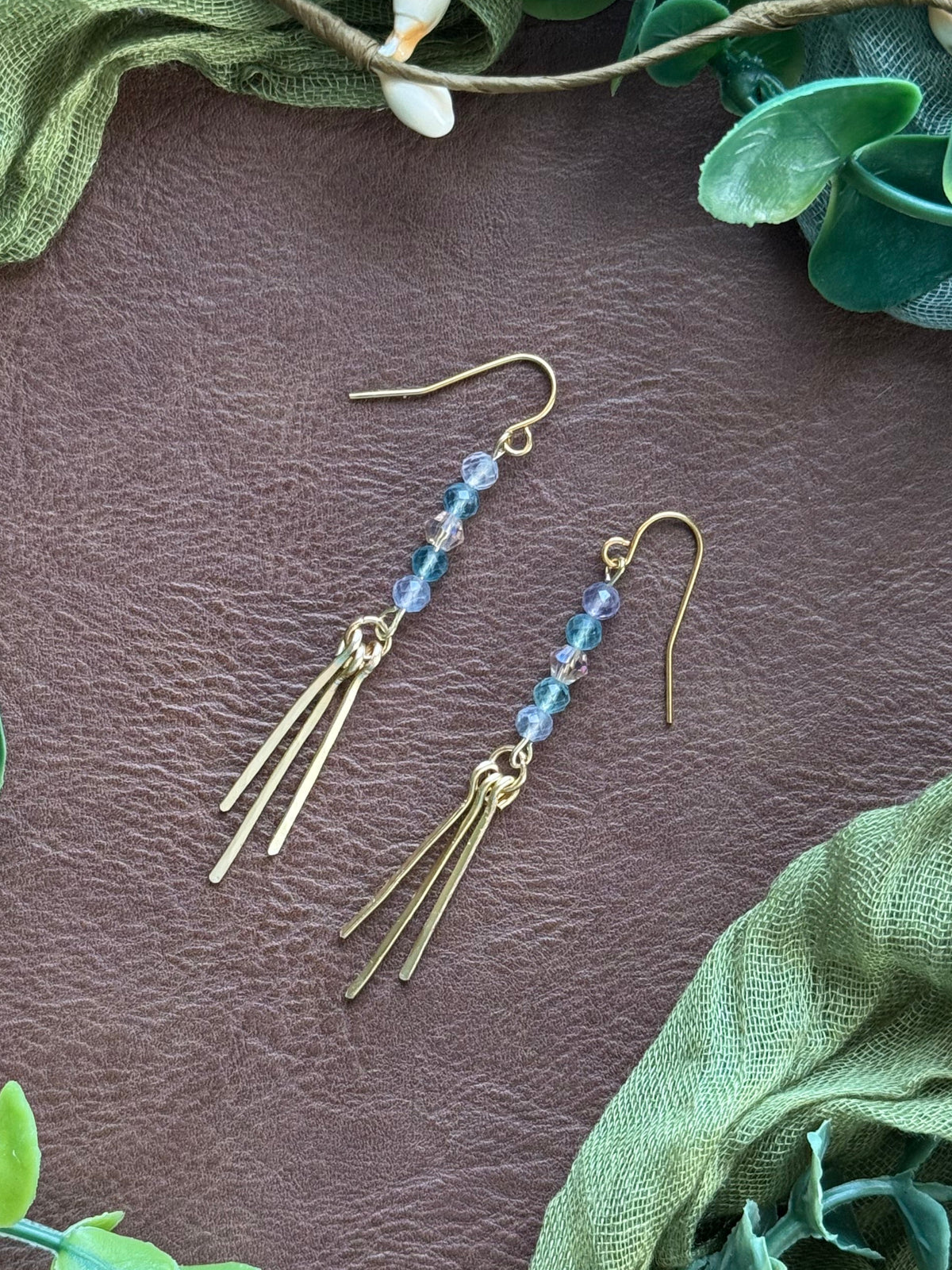 Handmade earrings featuring wire smithing techniques and gemstone beads on a natural surface with green leaves around.