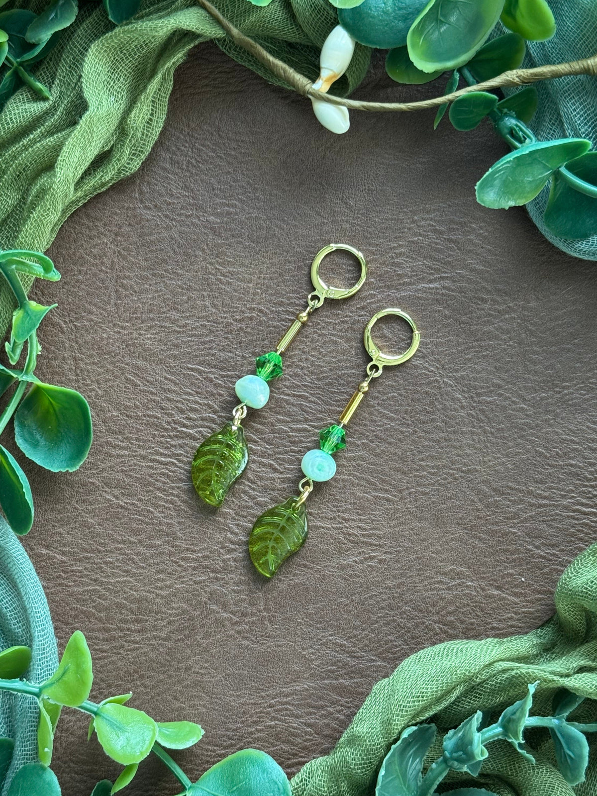 Handmade beaded earrings with pearl and glass beads on a natural background with green leaves around.