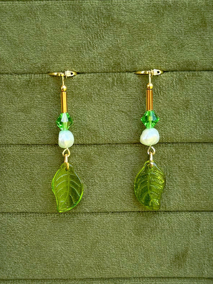 Handmade beaded earrings with pearl and glass beads, displayed on an olive green textured background.