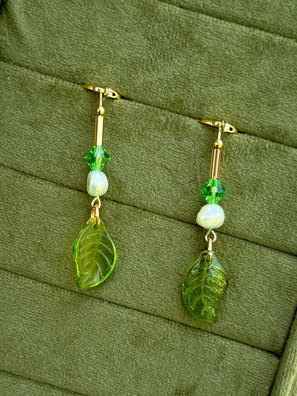Handmade beaded earrings with pearl and glass beads, displayed on an olive green textured background.