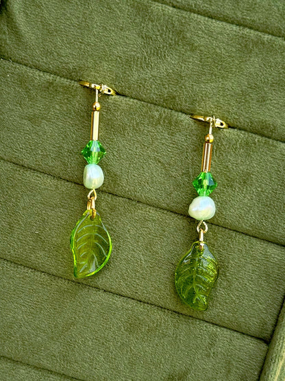 Handmade beaded earrings with pearl and glass beads, displayed on an olive green textured background.