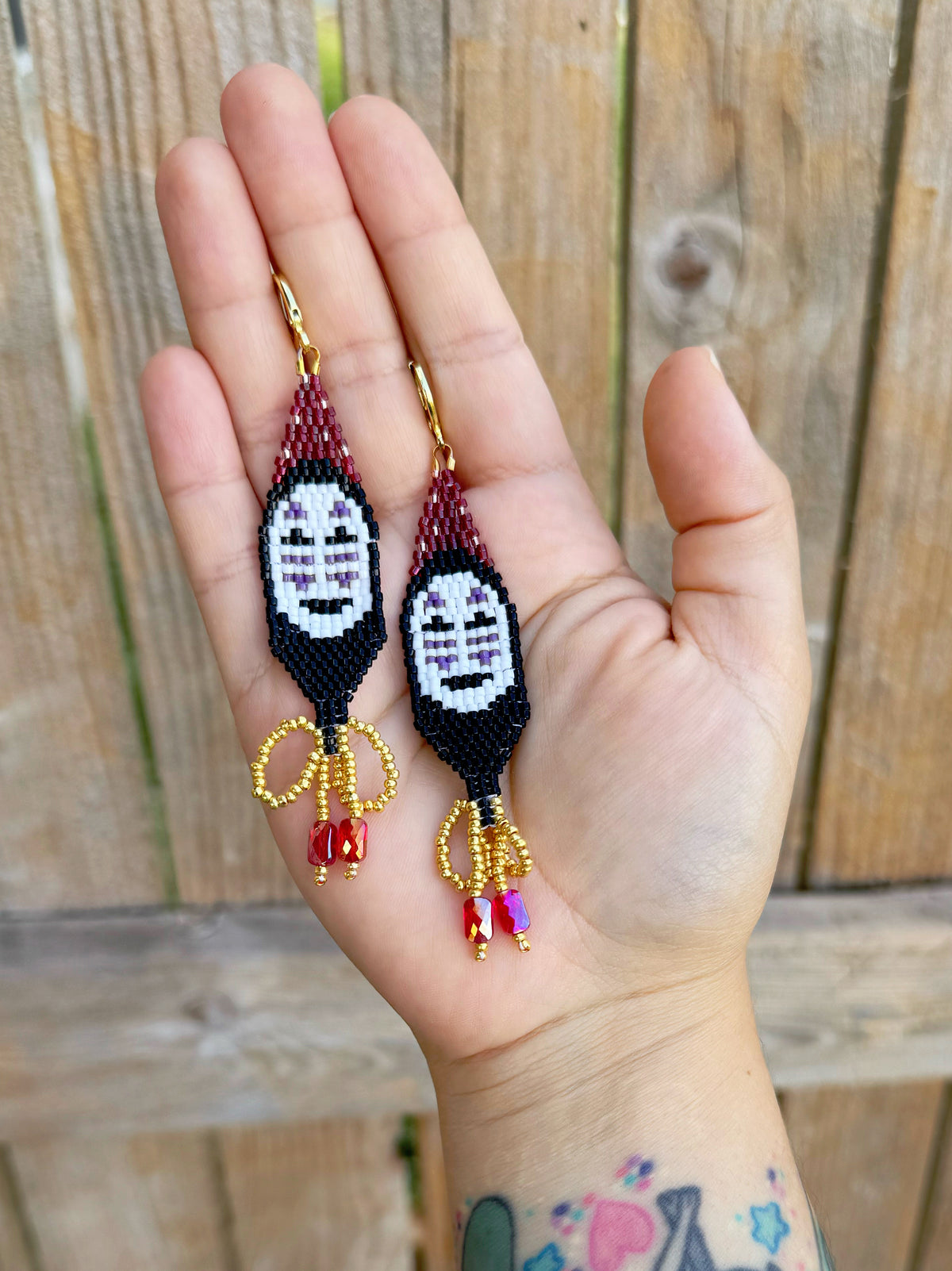 Handmade beaded earrings inspired by Spirited Away with a wooden fence background.