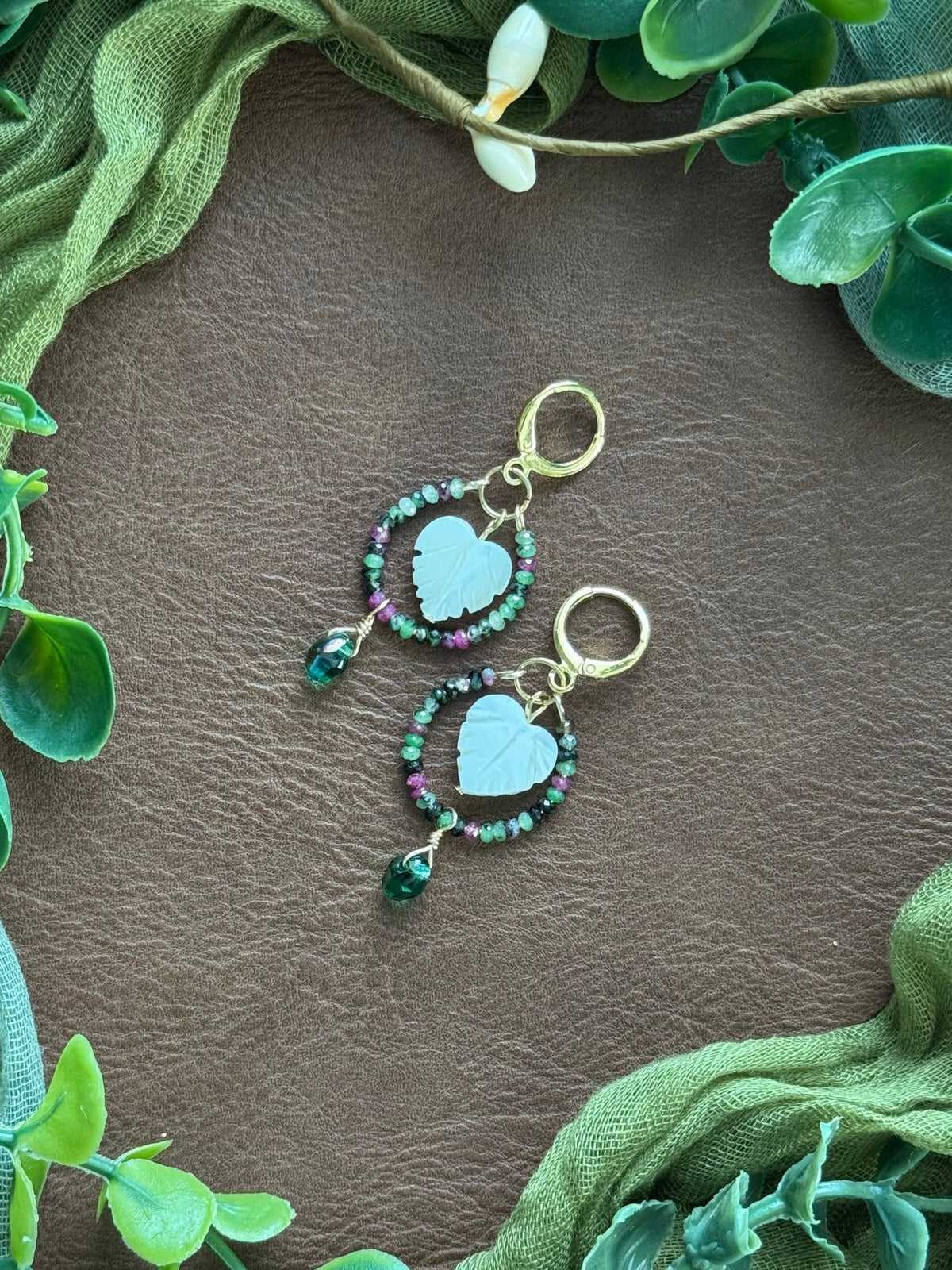Handmade beaded earrings with gemstone and Czech glass beads on a natural background with green leaves around.
