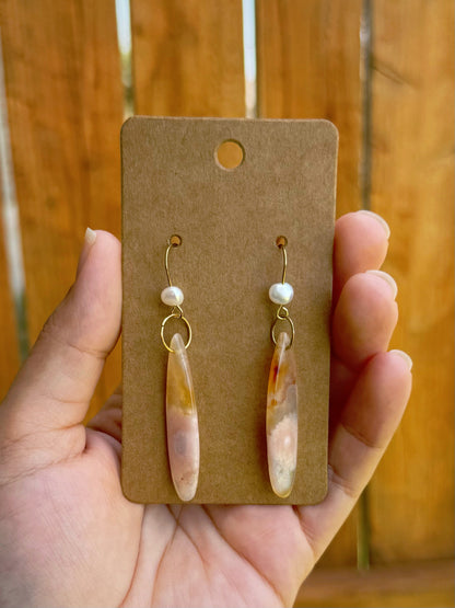 Handmade earrings with sakura agate teardrop beads, a dainty freshwater pearl, and gold ear hooks, on a kraft paper card.