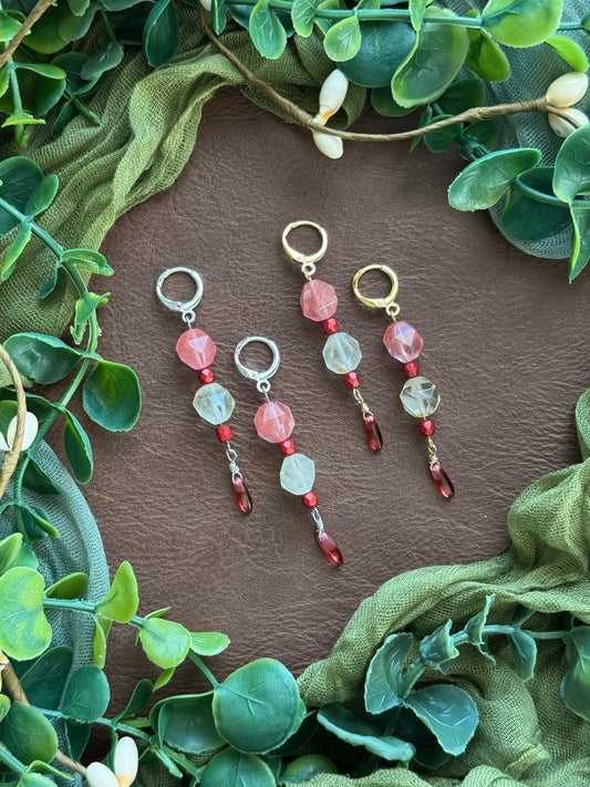 Collection of handmade beaded earrings with gemstone and Czech glass beads on a natural background with green leaves around.