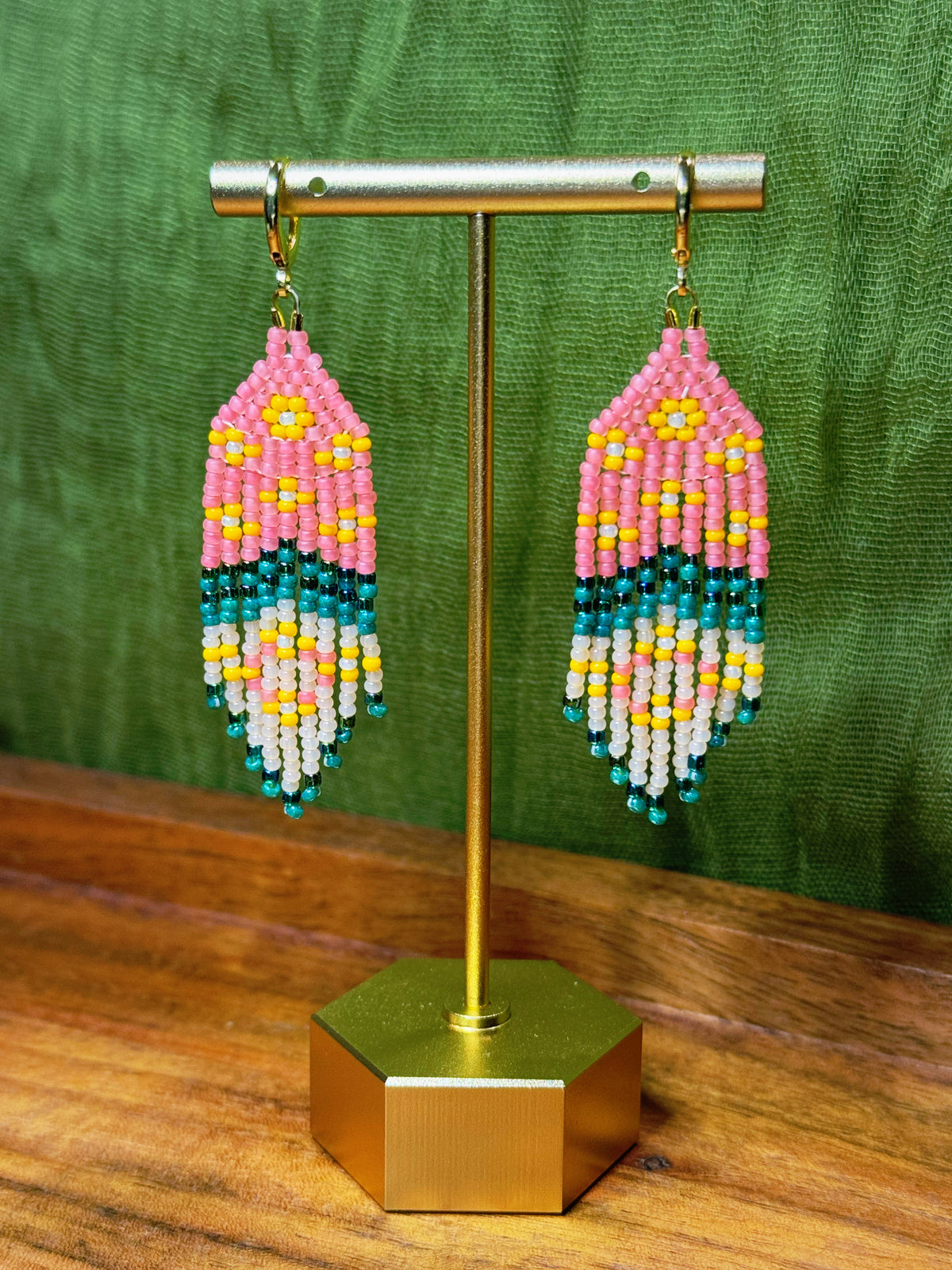 Beaded earrings on a gold stand with a green background.
