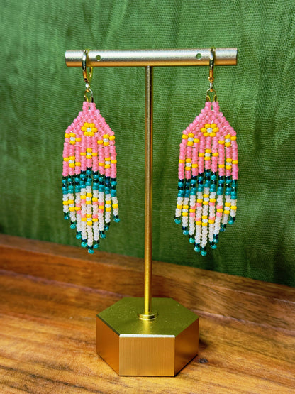 Beaded earrings on a gold stand with a green background.