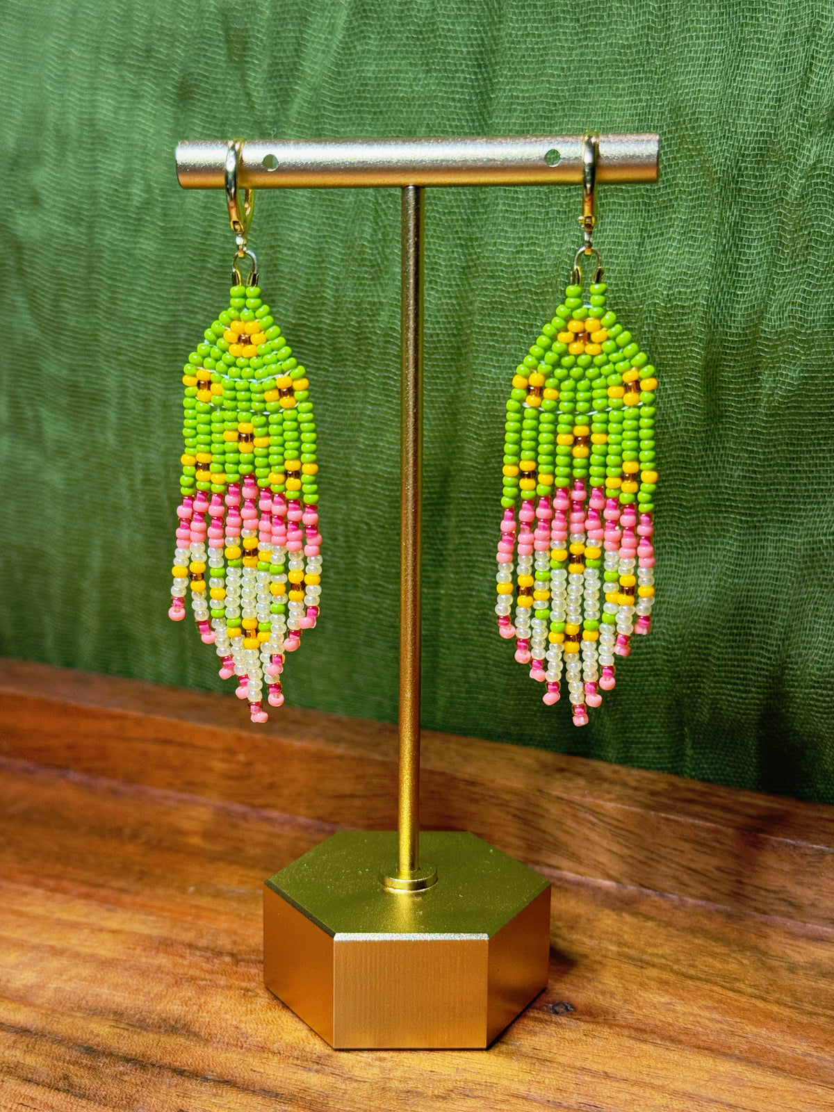 Beaded earrings on a gold stand with a green background.