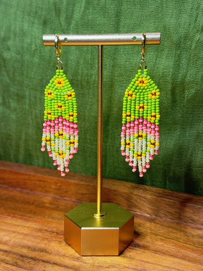 Beaded earrings on a gold stand with a green background.