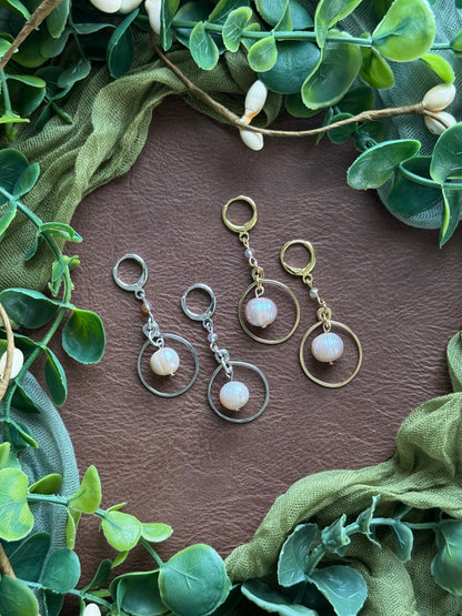 Collection of handmade beaded and wire-smithed earrings with pearl beads on a natural background with green leaves around.