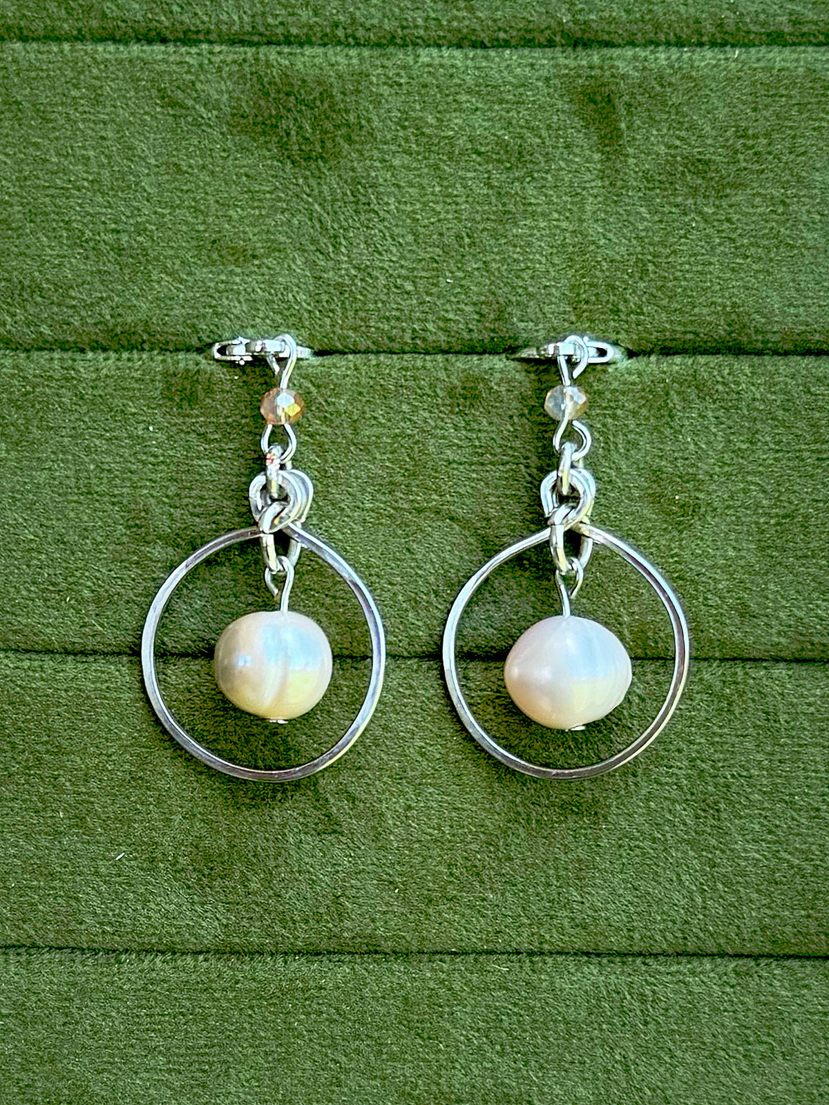 Handmade earrings with smooth, lustrous white freshwater pearls, displayed on a textured green velvet surface.
