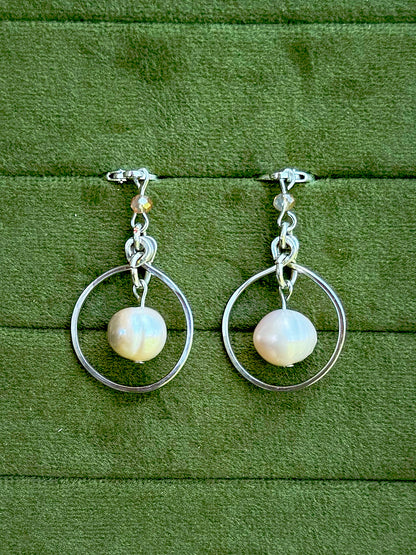 Handmade earrings with smooth, lustrous white freshwater pearls, displayed on a textured green velvet surface.