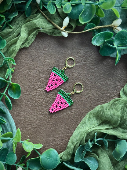 Handmade watermelon-themed beaded earrings using 11/0 glass seed beads on a natural surface with green leaves around.