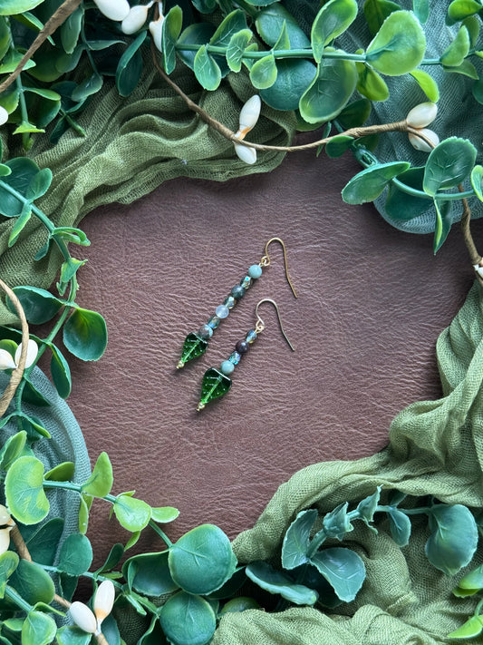 Handmade asymmetrical beaded earrings with gemstone and glass beads on a natural background with green leaves around.