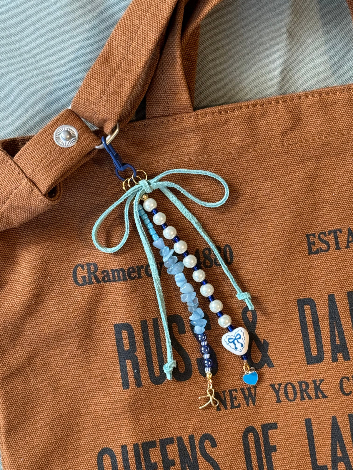 Handmade beaded bag charm keychain with a ceramic heart charm, blue quartz chip beads, and a blue suede cord bow.