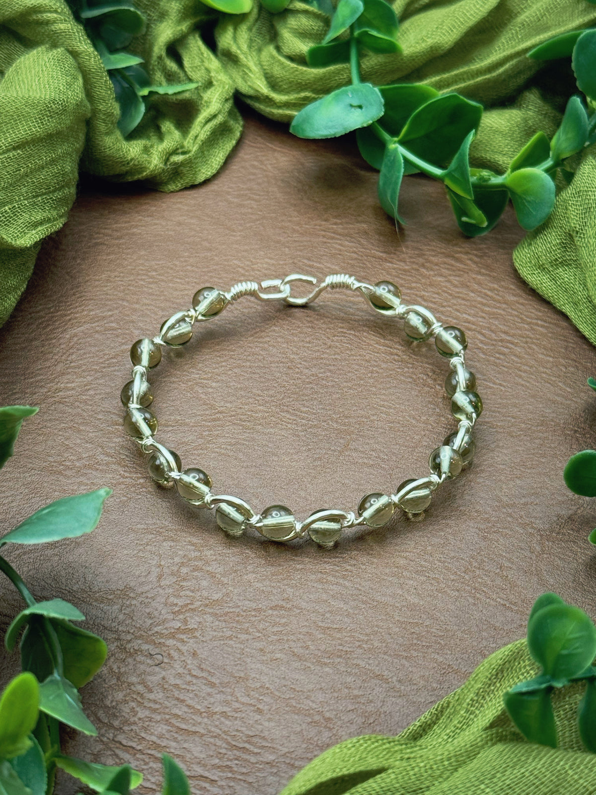 Handmade, wire-wrapped bracelet shaped like a wave, featuring smoky clear glass beads.