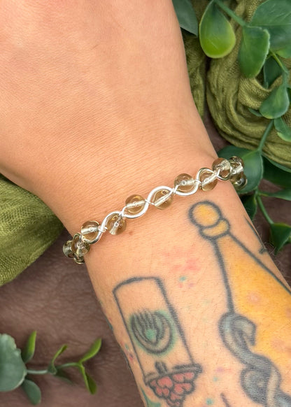 Handmade, wire-wrapped bracelet shaped like a wave, featuring smoky clear glass beads.