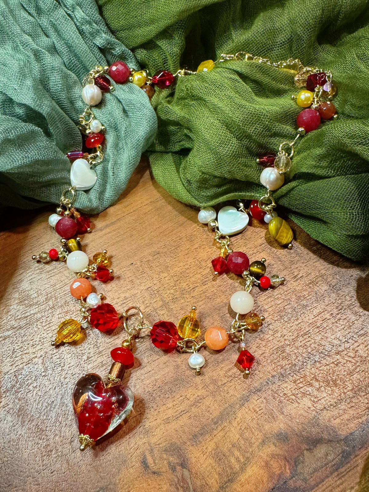Colorful beaded necklace with heart charm on a wooden surface with green fabric in the background