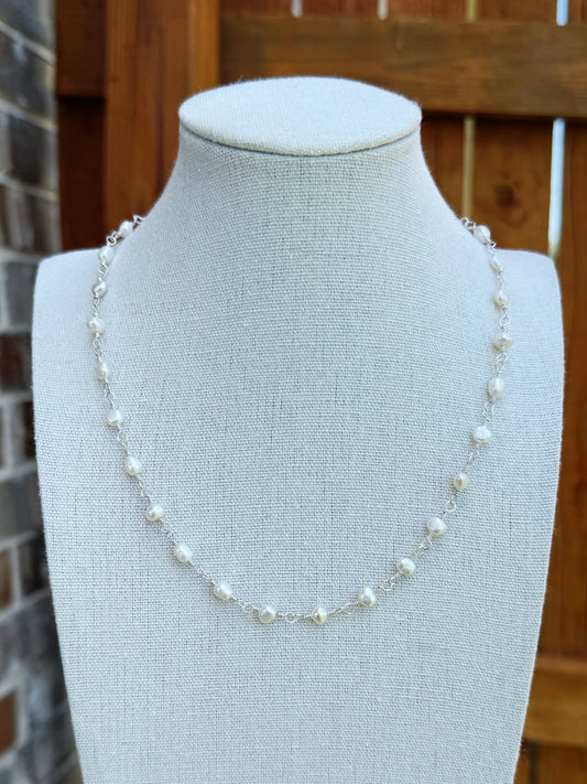 Handmade silver chain necklace with small white freshwater pearls, displayed on a fabric jewelry bust.