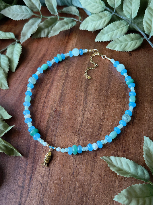 Necklace with blue beads and gold charm on a wooden surface with leaves