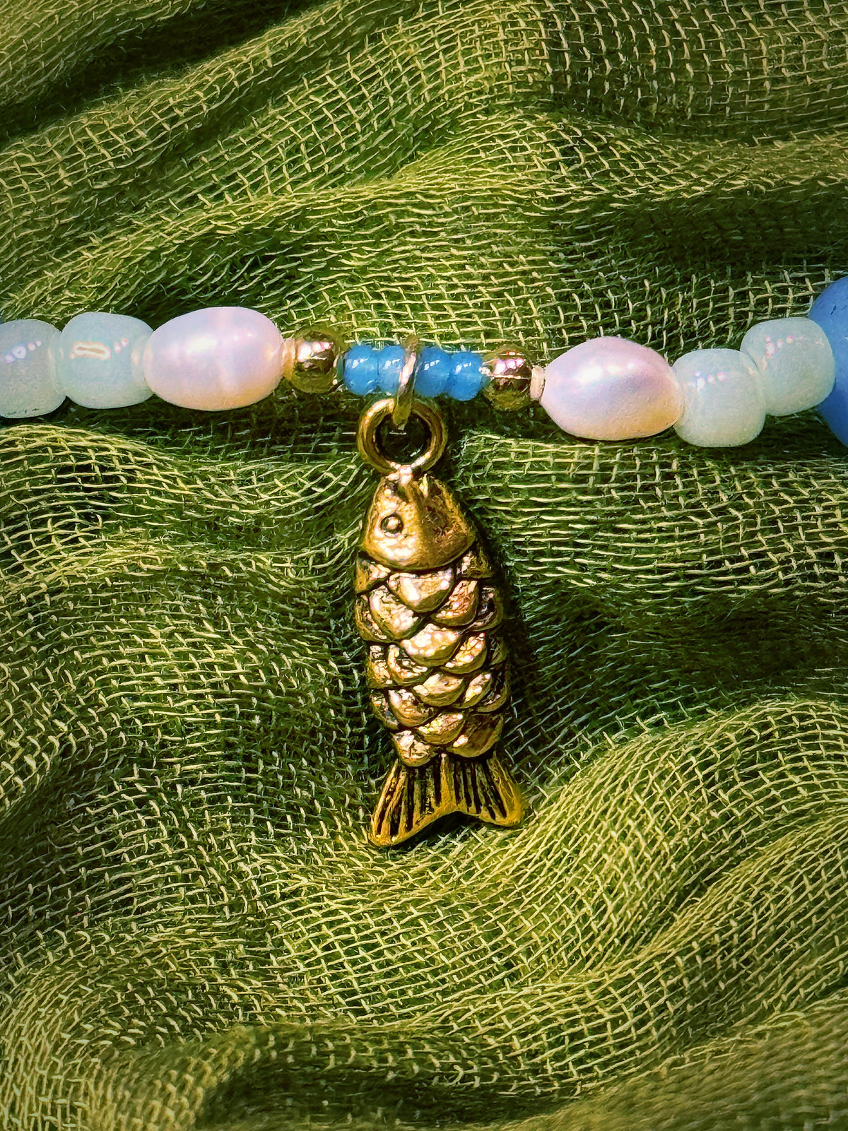 Bracelet with gold fish charm and colorful beads on a green fabric background