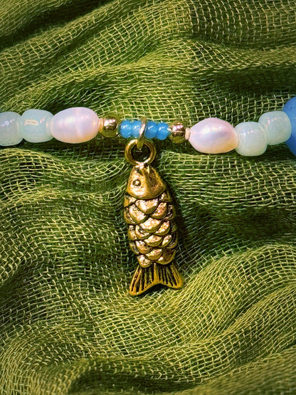 Bracelet with gold fish charm and colorful beads on a green fabric background